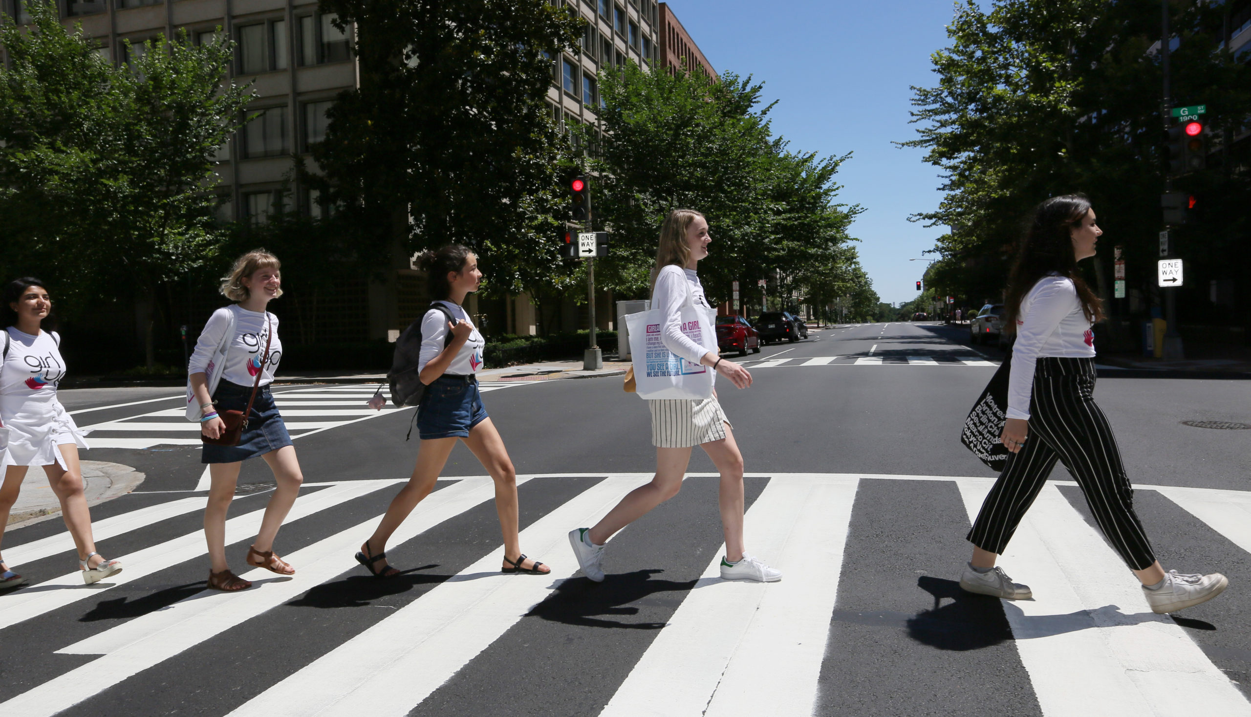 Cinco chicas cruzan la calle una tras otra mirando al frente con sus camisetas de Consejeras adolescentes.